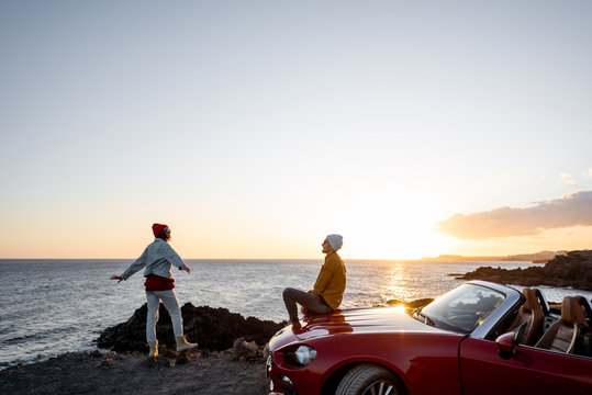 Couple having fun together, enjoying landscapes while traveling by car on the rocky coast, wide view from the side with copy space on the sky