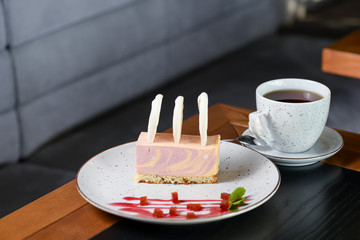 Ripe sea buckthorn mousse dessert with caramel biscuit served on a white plate with a cup of tea