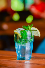 Classic fresh mojito on the table in a bar. Alcohol cocktail with ice, mint and lime on table with blurred background.