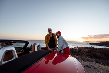 Young joyful couple having fun on the rocky coast while traveling by car on a sunset. Carefree...