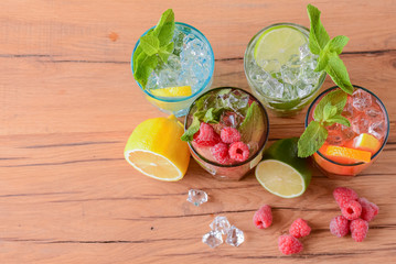 Four tropical mixed drinks, orange, lemon and raspberries cocktails over bright pastel green background.