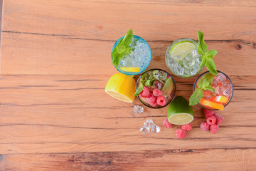 Four tropical mixed drinks, orange, lemon and raspberries cocktails over bright pastel green background.