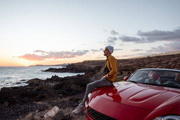 Lifestyle portrait of a man on the rocky coast during a sunset, traveling with woman by car