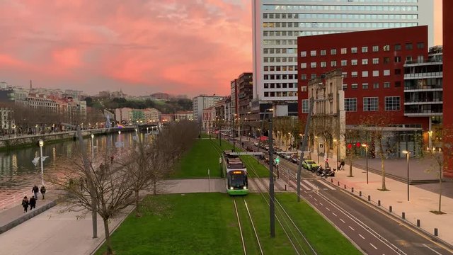 Bilbao city center with beautiful winter sunset sky; combination of modern and old architecture, green grass, public transportation system low-floor tram; developed urban environment
