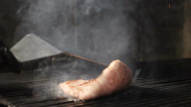 Cooking meat for hamburger on grill in slow motion. meat being turning using spatula. Steam rising up. Unhealthy fast food concept. hd footage