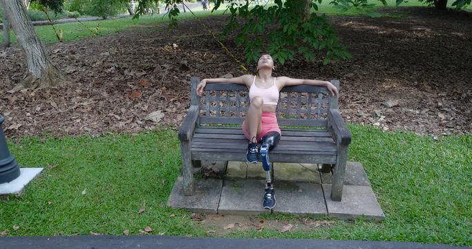 Leg Amputee Asian girl feeling stressful and thinking about her life in a park bench, slow motion clip