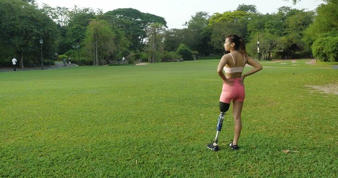 Leg Amputated Asian girl standing in a nature park after her workout session early in the morning