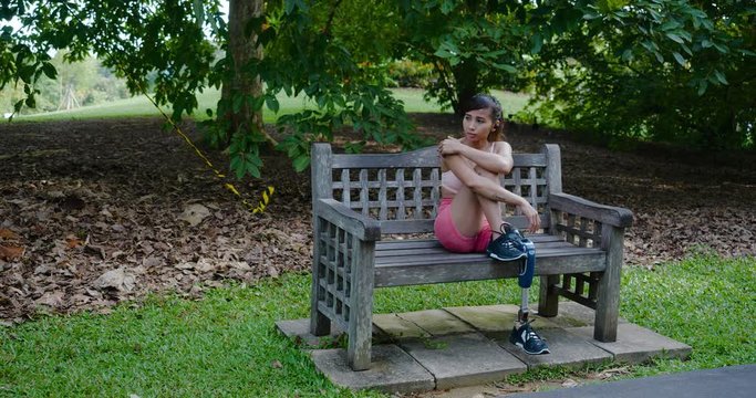 Leg Amputee Asian girl feeling sad and thinking about her life in a park bench , slow motion clip
