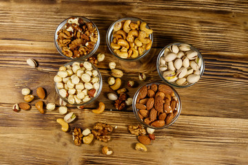 Assortment of nuts on wooden table. Almond, hazelnut, pistachio, walnut and cashew in glass bowls. Top view. Healthy eating concept