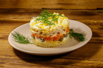 Tasty layered salad with potatoes, chicken breast, marinated mushrooms, carrots, eggs and mayonnaise on wooden table