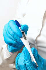 The doctors hands in gloves hold a white electronic thermometer closeup on a light background, checking the patients high temperature, symptoms of a virus or illness. Diagnosis of health.