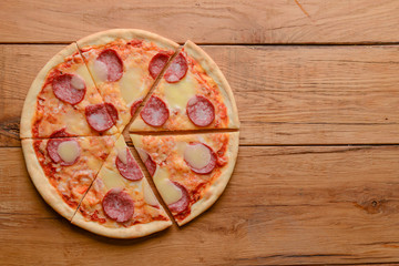 Flat lay pepperoni pizza isolated on rustic wooden background. Pizza salami cut in slices. Fast food, junk food concept.