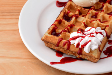 Plate of belgian waffles with ice cream and fruit strawberry caramel sauce on wooden table background