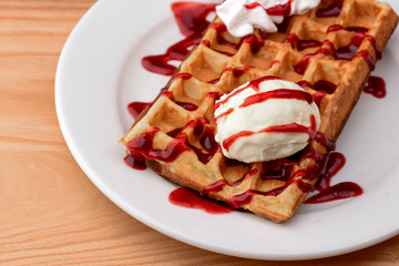Plate of belgian waffles with ice cream and fruit strawberry caramel sauce on wooden table background