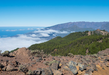 Volcanic landscape with lush green pine trees, colorful volcanoes and lava rock field along path Ruta de los Volcanes, hiking trail at La Palma island, Canary Islands, Spain, Blue sky background