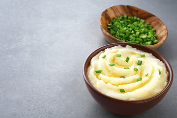 Bowl with mashed potatoes and onions on gray texture.