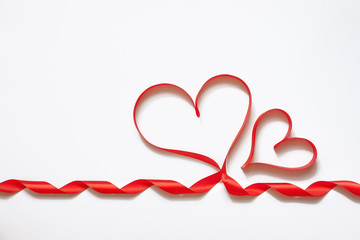 Shiny red ribbon on white background with copy space. Valentine Heart. Elegant red satin or silk gift ribbon.