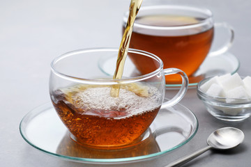 Hot tea poured into a cup on a gray background.