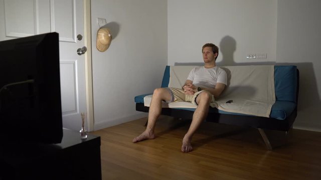 Young Man Sitting on Couch and Watching TV Alone at Night
