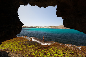 View from cave of woman in bikini exploring rugged limestone coastline on sunny day on the Great...