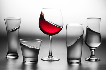 Some glasses of water in black and white and a glass of red wine