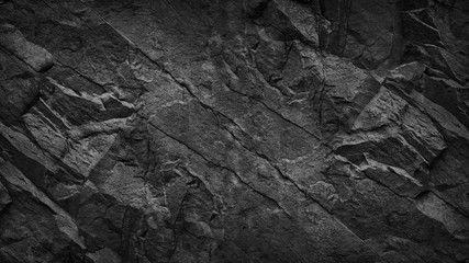 Black grunge background. Dark gray rock texture. Cracked rough stone surface. Mountain texture closeup. Black and white background. Volume. 3D effect.