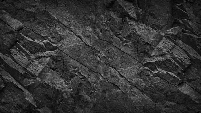 Black grunge background. Dark gray rock texture. Cracked rough stone surface. Mountain texture closeup. Black and white background. Volume. 3D effect.