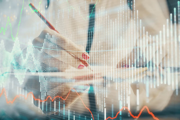 A woman hands writing information about stock market in notepad. Forex chart holograms in front. Concept of research.