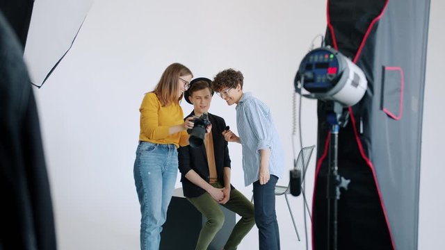 Slow motion of cheerful people model, make-up artist and photographer working in studio watching photos on digital camera and putting on makeup