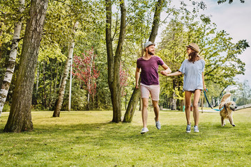 Young couple holding hands and running with dog in the park