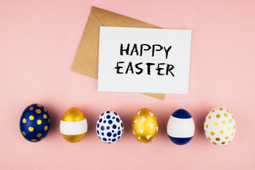 Modern golden blue spring easter eggs, envelope and letter with happy easter phrase flat lay on colorful pink background top view copy space. Easter celebration concept template. Stock photo.
