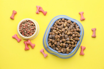 Bowls with dry pet food on color background