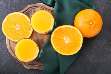 Glasses of fresh orange juice and fruit on dark background