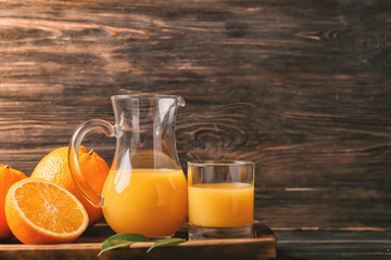 Jug and glass of fresh orange juice on wooden background