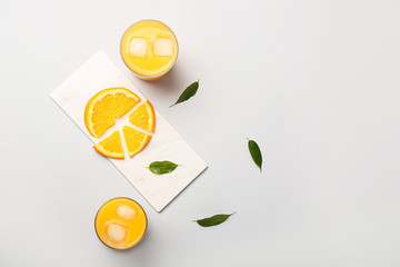 Glasses of fresh orange juice and fruit on light background