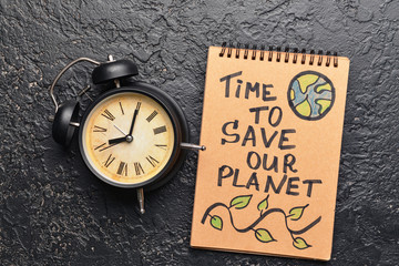 Notebook with text TIME TO SAVE OUR PLANET and clock on dark background