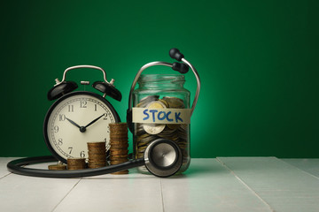 conceptual money growing, increasing finance situations, time cost money, finance checking. stacked money coins, a clock and a glass bottle of coins with a stethoscope againt green background