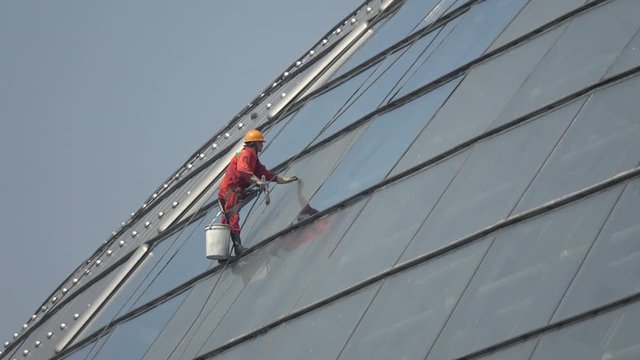 Aerial view of man window washing is exterior cleaning of architectural glass used for structural lighting in this case done manually using a variety of tools for cleansing and access 4k quality