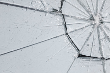 A shattered glass on a light surface, ripped in big pieces like a cobweb, many sharp fractured...