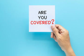 hand holding paper with question ARE YOU COVERED? isolated on blue background with copy space. travel insurance concept