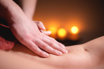 Men's premium luxury hip massage anti-cellulite wellness center. Close-up of a male masseur doing leg massage to a female client in an office with dark light on a background of burning candles