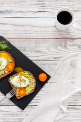Sandwich with poached egg, avocado, cherry tomatoes, micro greens and wholegrain bread on feed board. Healthy delicious breakfast or lunch concept.