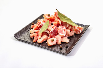 Diced raw pork meat, isolated on white background. Fresh pieces, dry bay leaf on black ceramic plate