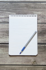 Notepad with a blank white sheet in a checker paper with ball pen lies on the background of wooden boards