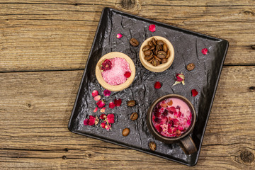 Trendy colored latte. Rose petals and powdered aromatic sugar, coffee beans. Wooden boards background