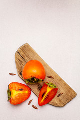 Ripe single persimmon. Fresh whole fruit, half sliced, seeds. Wooden cutting board, stone concrete...