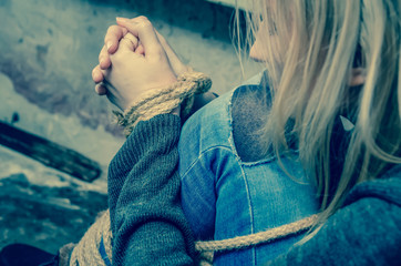 blonde girl with her hands and feet tied is sitting in the basement. Concept of kidnapping, violence