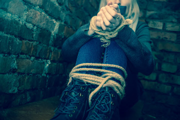 girl with her hands and feet tied and her mouth taped up is sitting in the basement. Concept of...