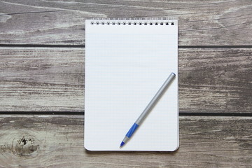 Notepad with a blank white sheet in a checker paper with ball pen lies on the background of wooden boards