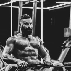 Fototapeta na wymiar Young strong bearded bodybuilder doing low cable pulley row seated, dramatic black and white image